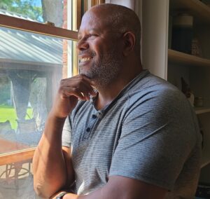 Cecil Archbold voice actor standing at a window with natural light with a confident, relaxed expression
